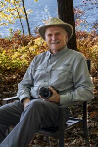 photo of Brien Richards sitting in a chair outside holding a camera
