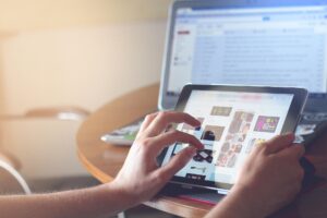 image of laptop and tablet on a table with person using it but only hands are seen